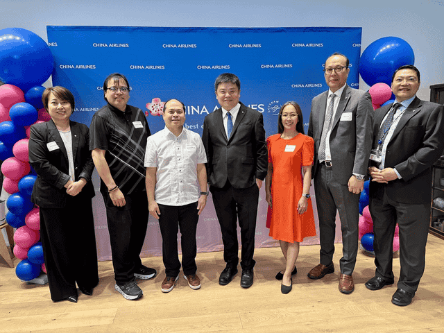 Eight adults in business attire pose for a group photo in front of a blue China Airlines backdrop with pink and blue balloons on either side.